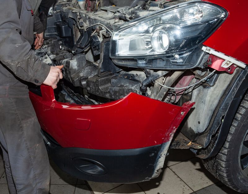 Auto body technician installing body parts on a car frontend.